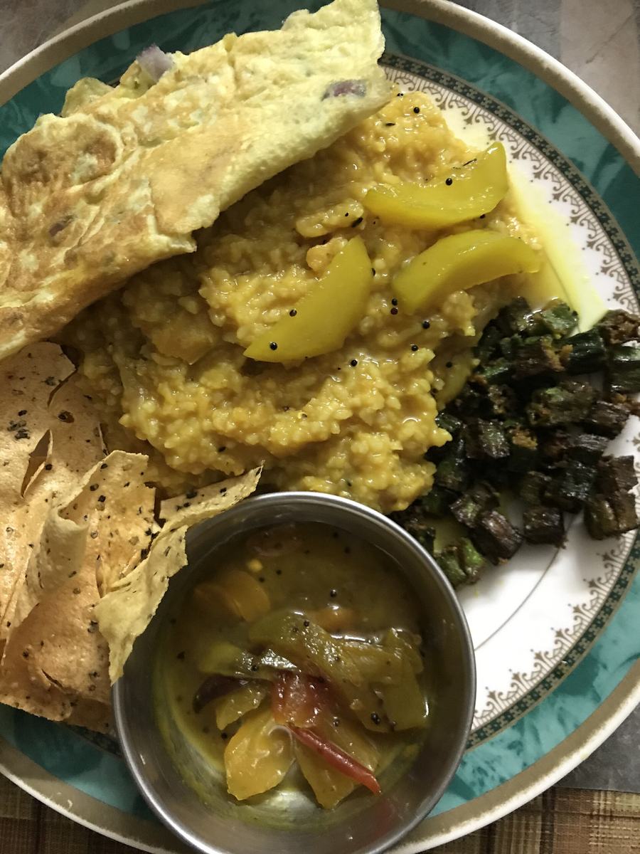A plate of khichuri with papad, fried vegetables and chutney