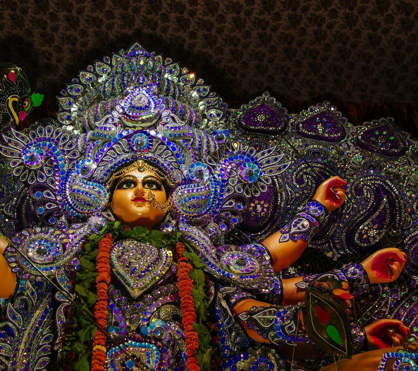 The goddess Durga in a pandal, seen from below, her face lit and her crown glittering