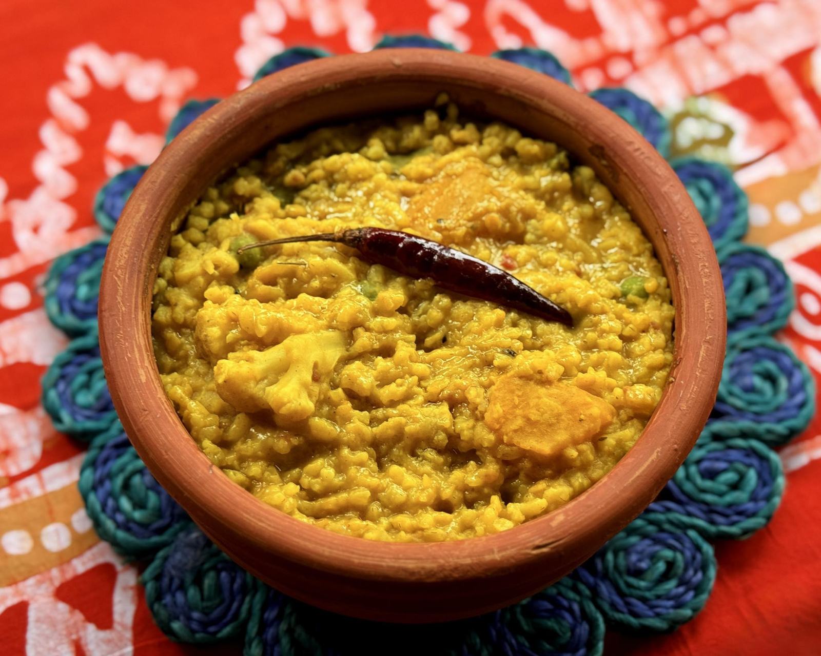 Yellow khichuri in a clay bowl with a dried red chilli on top